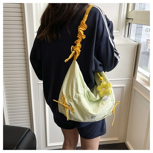 Dettaglio borsa a mezzaluna in nylon verde chiaro con tracolla gialla e ciondolo a fiore