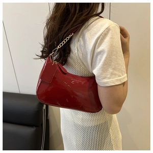 Detail of red patent leather baguette bag with crescent shape and gold chain strap
