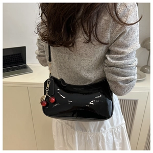 Detail of black patent leather shoulder bag with cherry charm and smooth zipper