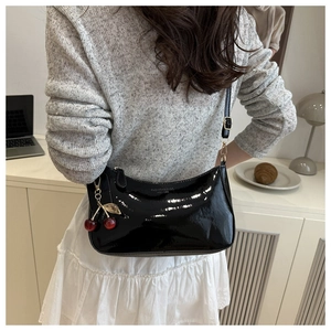 Detail of black patent leather shoulder bag with a red cherry charm and gold metal zipper