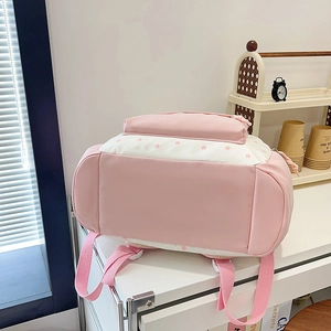 Pink and white school backpack with star patterns on a desk in a cozy room setting