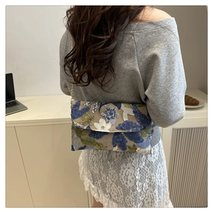 Dettaglio dei ricami floreali e paillettes su una pochette a busta in paglia con catenina