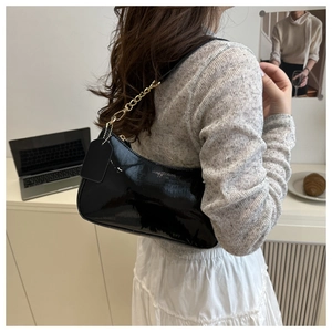 Close-up of black patent leather hobo bag with gold chain strap and hanging tag detail