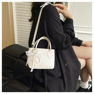 Close-up of white pebble leather bucket bag with pearl lace bow and slim shoulder strap