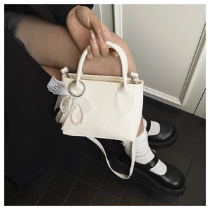 Detail of creamy white crossbody bucket bag with pearl strap and lace bow charm
