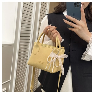 Mirror selfie showing a yellow textured crossbody bag with pearl lace bow charm