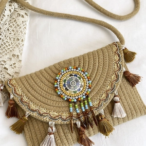 Bohemian straw crossbody bag with ethnic fringes and beaded mandala detail on white fabric
