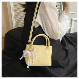 Detail of yellow lychee-textured leather bag featuring a pearl lace bow and logo