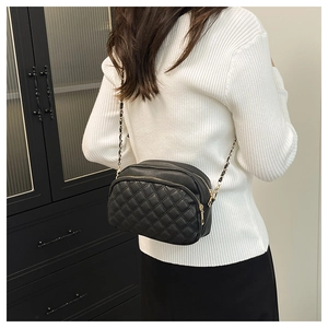 Detail of a black quilted crossbody bag with gold chain strap shown on a model