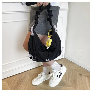 Dettaglio borsa a tracolla in nylon nero plissettato con fiocchi viola e ciondolo a fiore