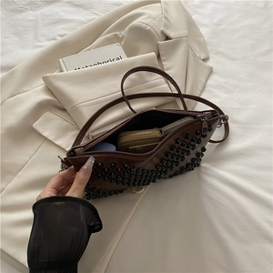 Brown leather shoulder bag with black studs on a beige blazer, urban retro style