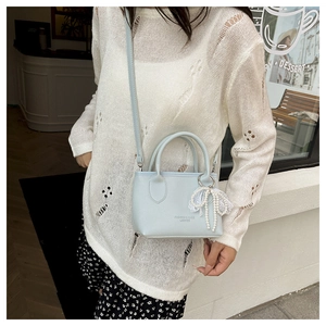 Detail of light blue mini bucket bag featuring a delicate lace bow and pearl pendant charm