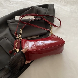 Red patent leather underarm bag with gold chain strap and cherry charm on grey blazer