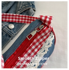 Detail showing smooth zipper and lace trim on denim handbag with red plaid strap