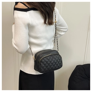 Detail shot of a black quilted crossbody bag with double zippers and gold chain strap