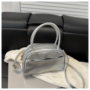 Detail der silbernen Metallic-Handtasche mit Tragegriffen und goldfarbenen Metallbeschlägen