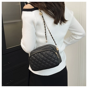 Detail of black quilted crossbody bag with dual zippers and gold chain strap adjustment