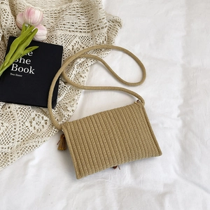 Handwoven straw crossbody bag with tassels on white lace background for summer vacations
