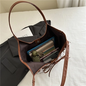 Ampia borsa tote con stampa mucca e manici marroni che mostra spazio per tablet e libri