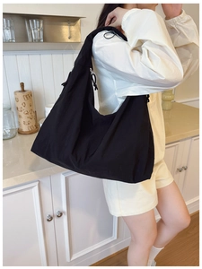 Large black shoulder bag with drawstring pleats worn by model in a bright kitchen setting