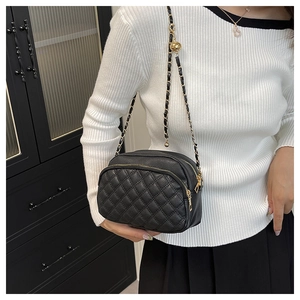 Detail of black quilted leather camera bag with gold chain strap worn by a model