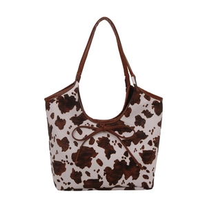 Chic cow print tote bag with bow detail and brown leather handles on white background