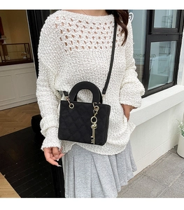 Detail of black quilted crossbody bag featuring a golden key pendant and arched handle