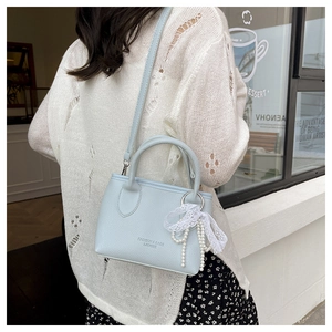 Close-up of light blue leather bucket bag with lace pearl bow decoration and shoulder strap