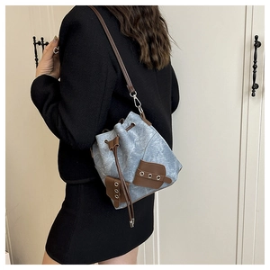 Detail view of light blue denim bucket bag with brown leather drawstring and straps