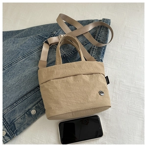 Detail of beige nylon crossbody bag showing metal logo and adjustable wide shoulder strap
