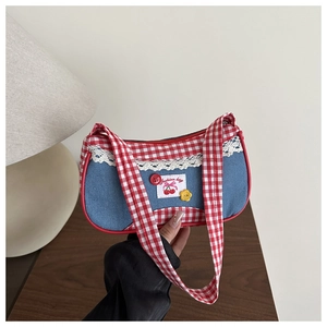 Detail of blue denim shoulder bag featuring red plaid straps and white lace trim detail