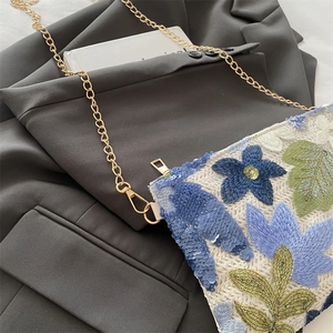 Woven crossbody bag with blue sequin floral patterns and a gold metal chain strap