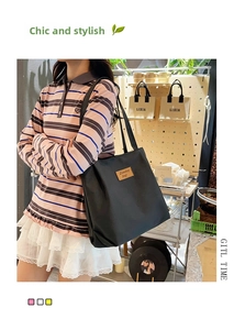 Detail of the black canvas tote bag showing the brown leather logo patch and soft texture