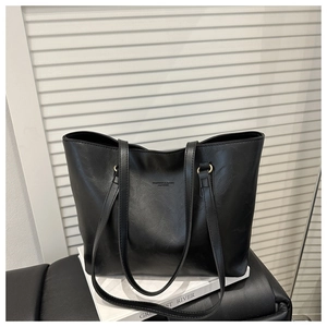 Detail of minimalist black faux leather tote bag with subtle gold logo on white surface