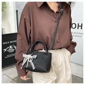 Detail of black lychee texture handbag featuring a pearl lace bow charm and crossbody strap