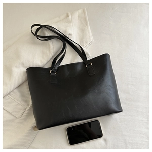 Flat lay of black PU leather tote bag with logo detail and smartphone for size reference