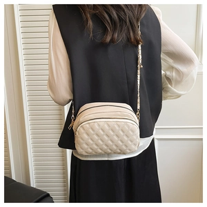 Detail of beige quilted crossbody bag featuring dual metal zippers and gold chain strap