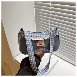 Detail of blue plaid underarm bag featuring delicate lace trim and cherry logo patch