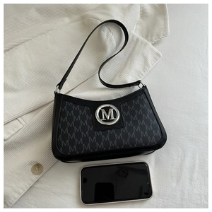 Detailed view of black baguette bag with M-letter monogram pattern next to a smartphone