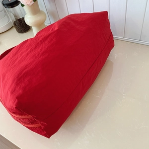 Large red nylon tote bag with bottom zipper compartment on stone background