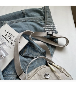 Detail of grey nylon crossbody bag with wide woven strap and metal logo on denim texture