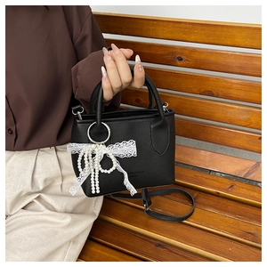Detail of black lychee leather bag with pearl lace bow and embossed fashion logo