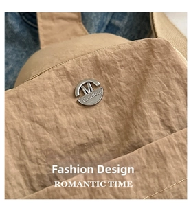 Detail of khaki nylon fabric texture with metallic decorative button and M Fashion logo
