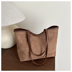 Detailed view of the brown suede tote bag on a wooden desk next to a modern desk lamp