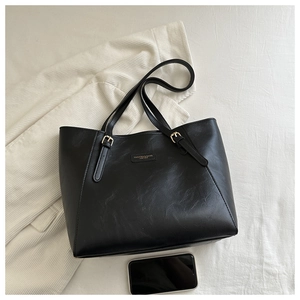 Detailed top view of black leather tote bag with gold buckle and fashion text detail