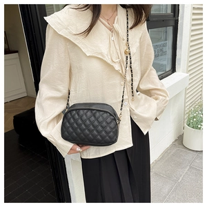 Detail of black quilted leather camera bag with golden ball chain and zipper closure
