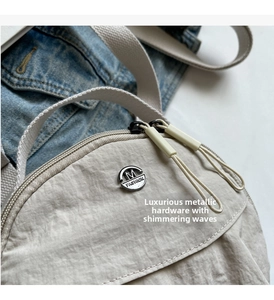 Detail of light beige nylon bag with dual zippers and circular M FASHION metal logo