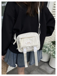 Close-up of white nylon crossbody bag with buckle straps and fashion logo patch