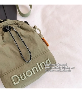 Détail du sac bandoulière en nylon vert montrant la broderie Duoning et l'étiquette orange