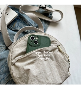 Macro detail of round beige nylon bag front zipper pocket showing smartphone storage space